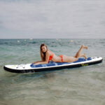 Chica joven descansando sobre tabla de paddle surf en el mar